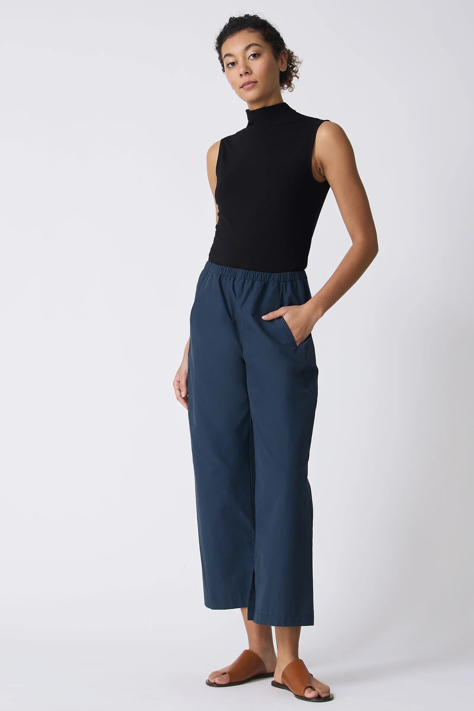 Woman wearing a black sleeveless top and blue pants on a white background.