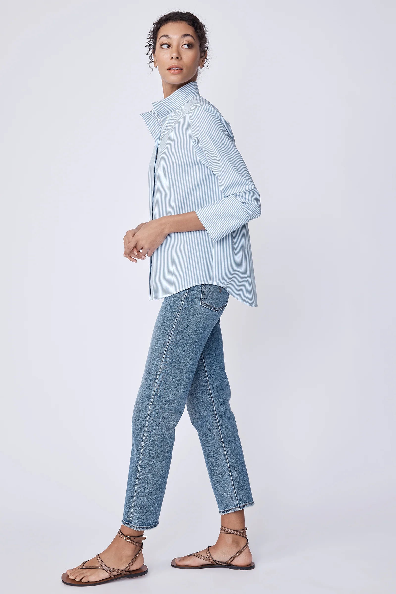Woman wearing a light blue stripe shirt and jeans on a white background.
