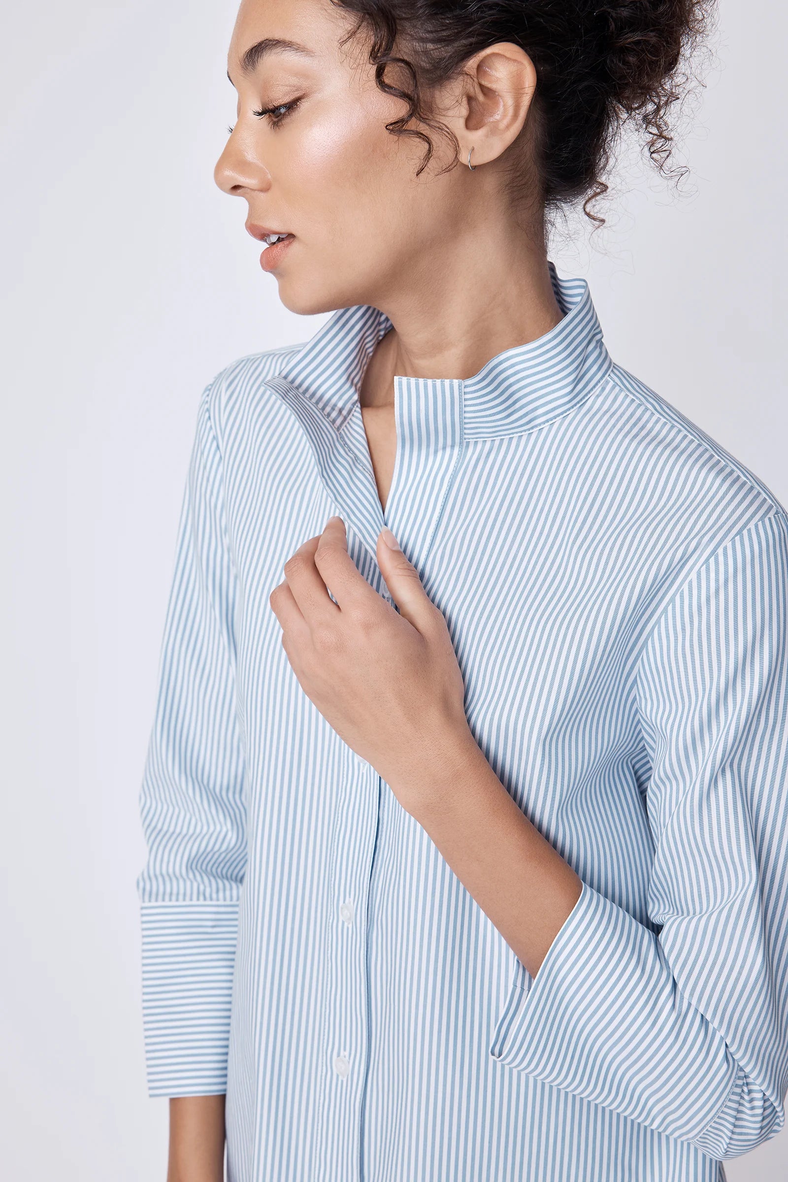 Close up of a woman wearing a light blue and white striped shirt against a plain background.