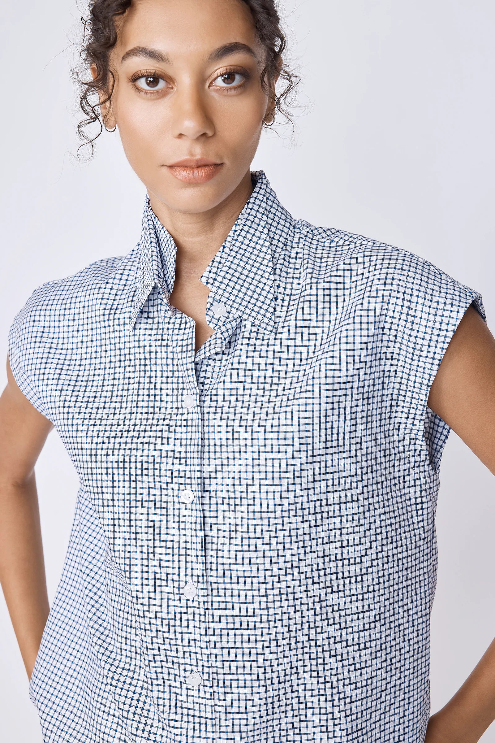 Woman wearing a sleeveless checkered shirt against a plain background.