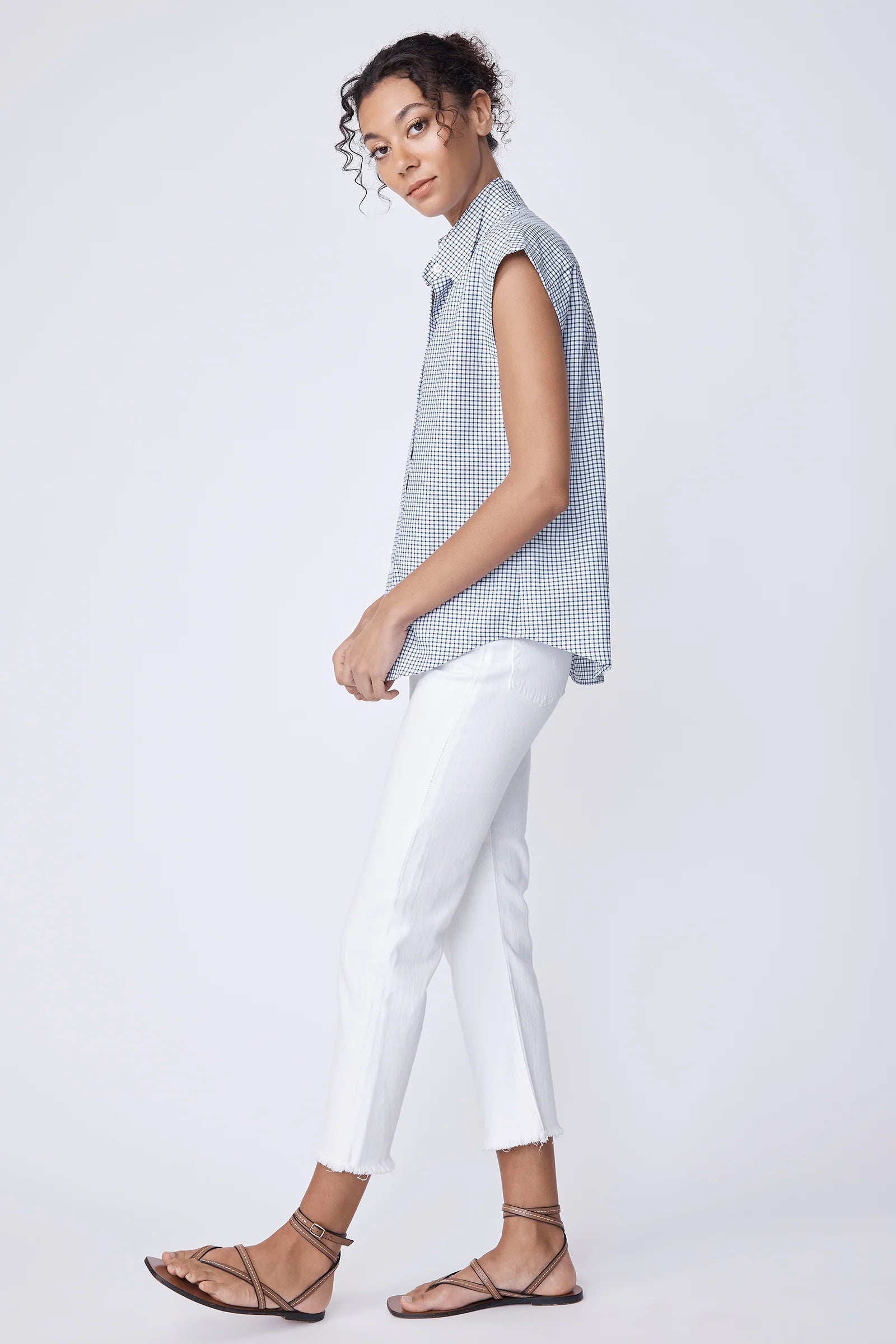 Woman wearing a sleeveless checkered top and white pants on a plain background.