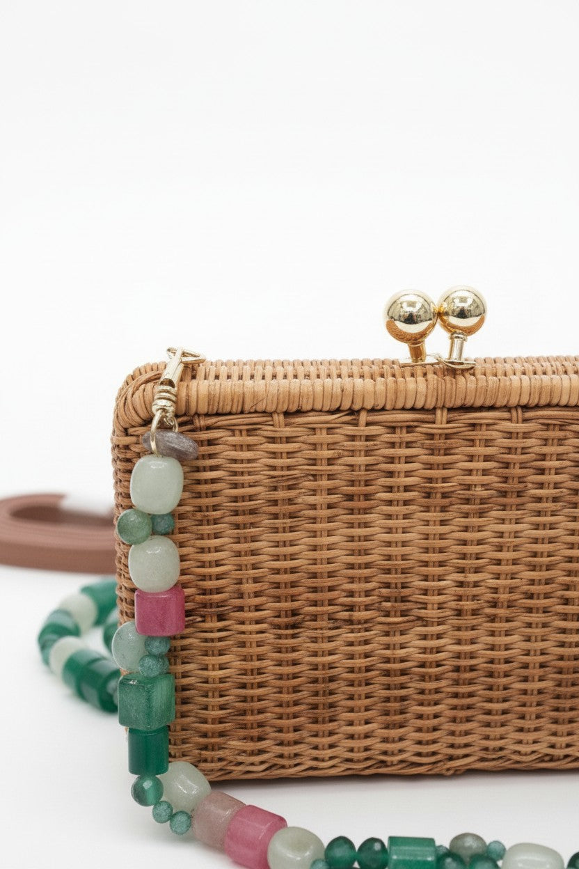 Close-up of a wickered clutch bag with a green beaded strap on a white background.
