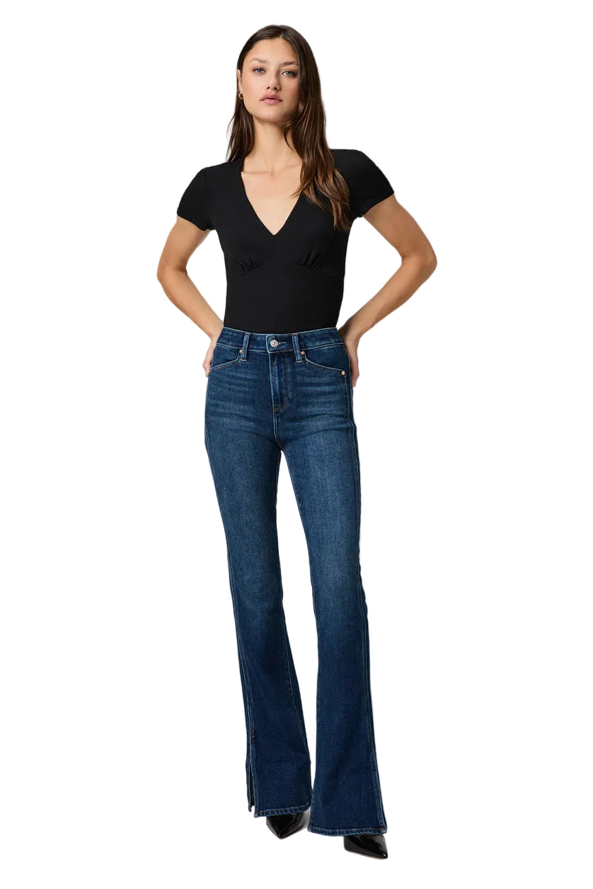 Woman wearing a black top and blue flared jeans on a white background.