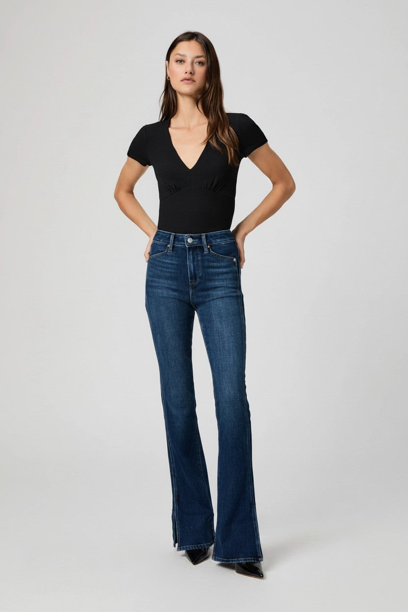 Woman wearing a black top and blue flared jeans on a white background.