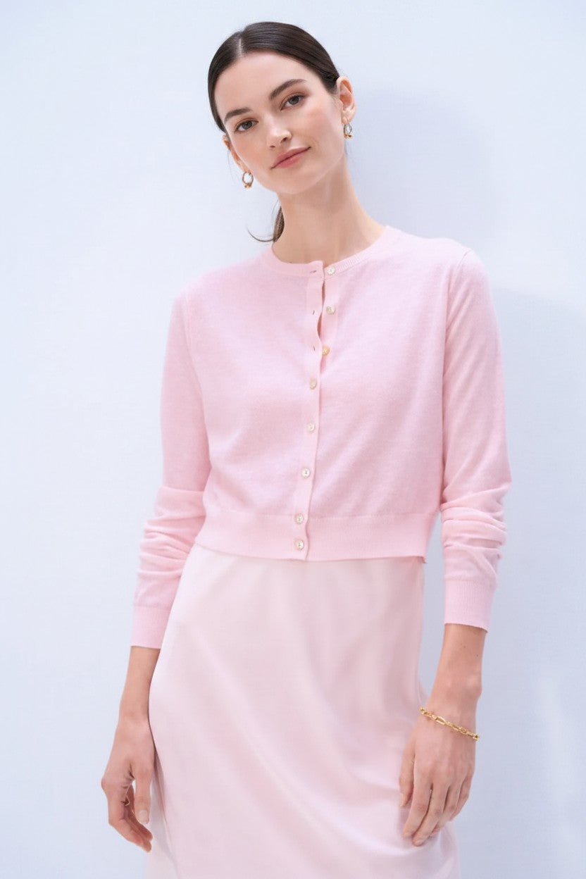 Woman wearing a light pink cardigan over a matching dress against a light background.