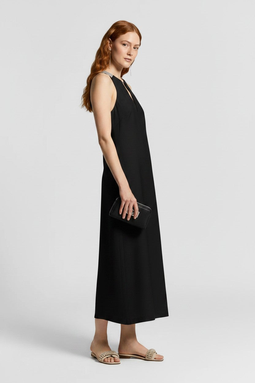 Woman posing in a black linen dress holding a black clutch and wearing gold sandals.