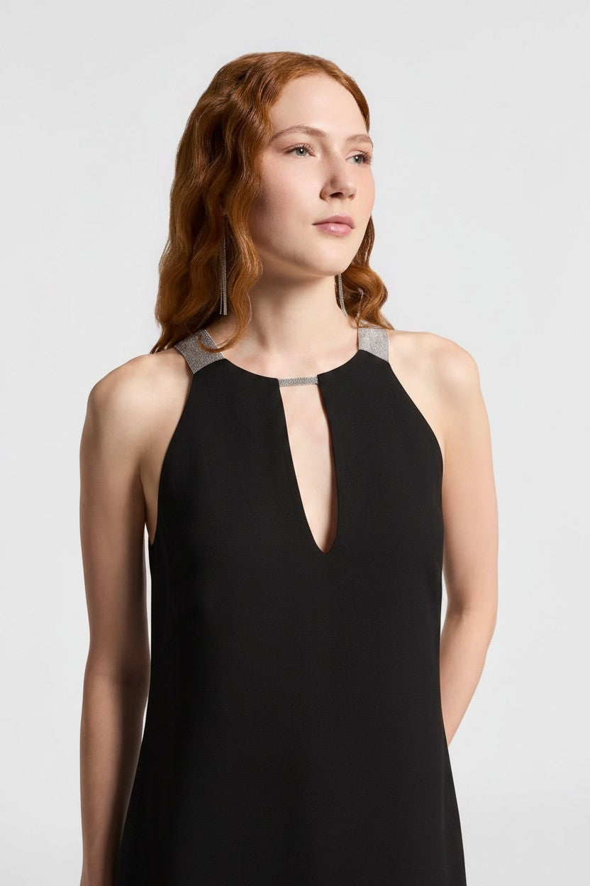Close-up of a woman wearing a black sleveless dress with a cut out on the chest and sparkle detailing along the neckline.