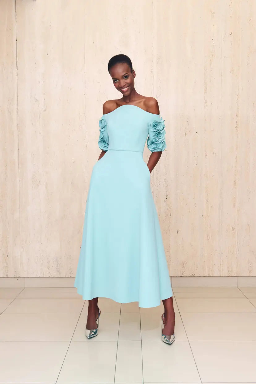 Woman wearing a light blue off-shoulder dress with floral sleeves against a wooden background