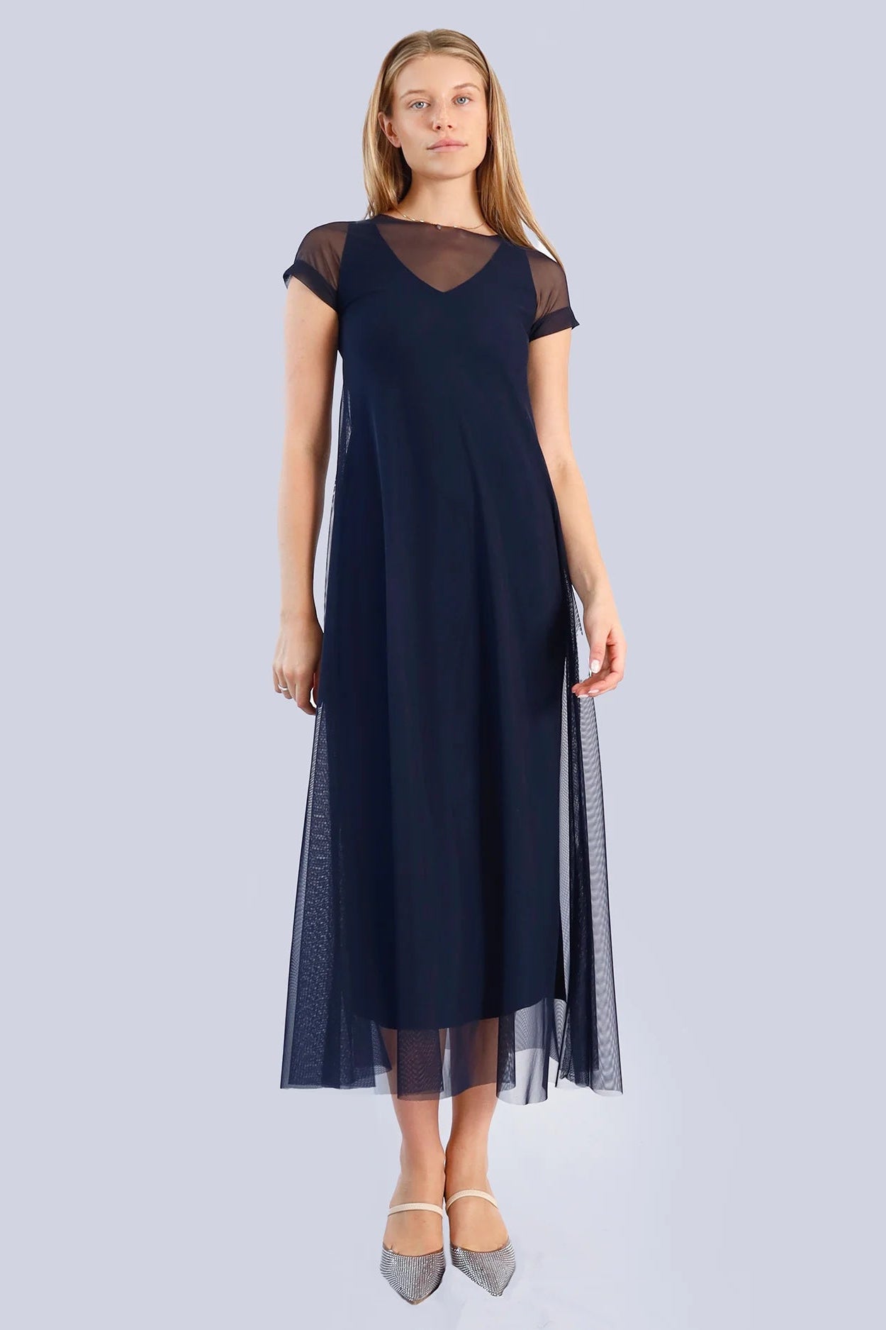 Woman wearing a navy short sleeve dress with sheer overlay on a plain background.