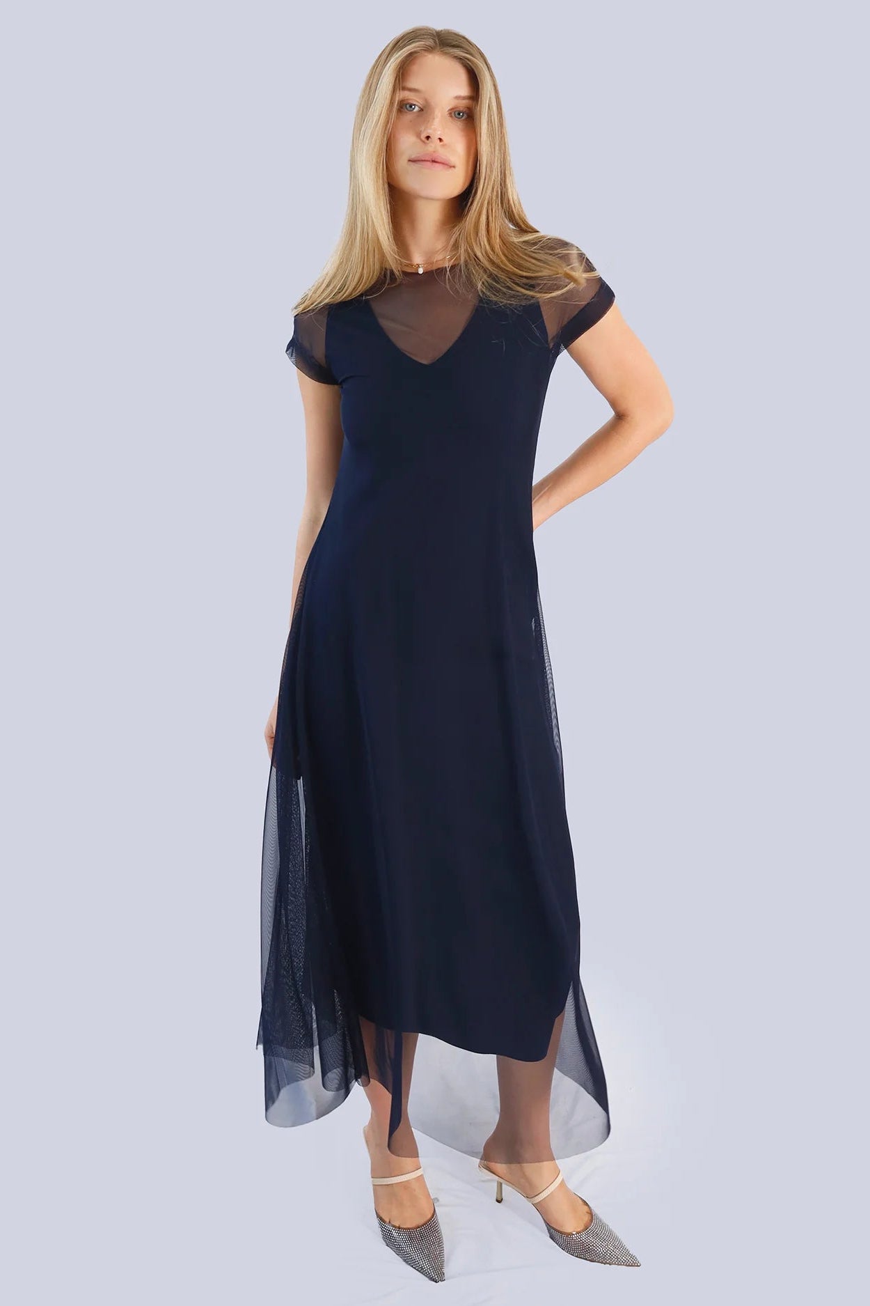 Woman wearing a navy blue dress with sheer sleeves on a light gray background.
