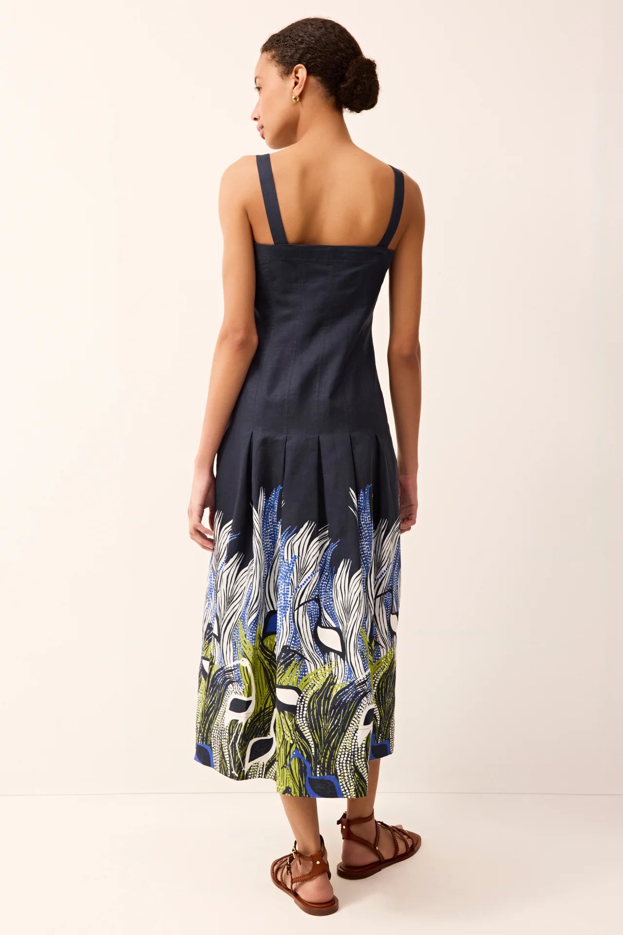 Back of a woman wearing a navy dress with a colorful feather pattern on a plain background.