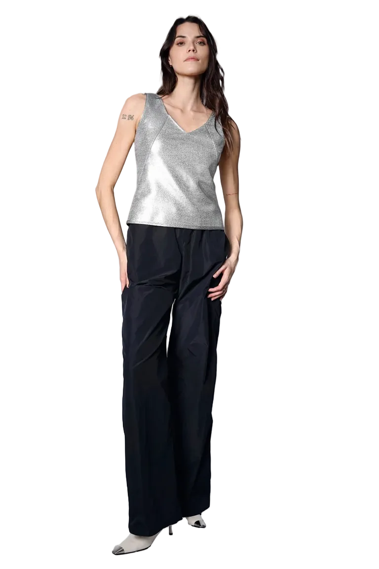 Woman wearing a silver sleeveless top and black wide-leg pants on a white background.