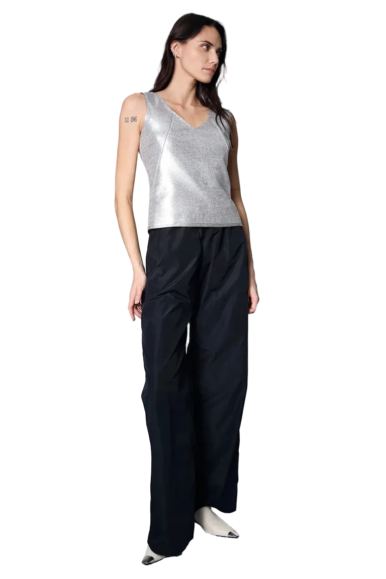 Woman wearing a silver sleeveless top and black pants on a white background