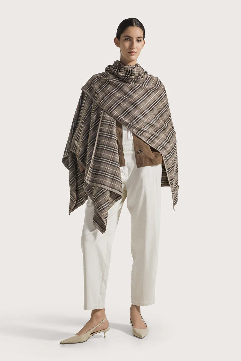 Woman wearing a plaid shawl over a white outfit on a light gray background.