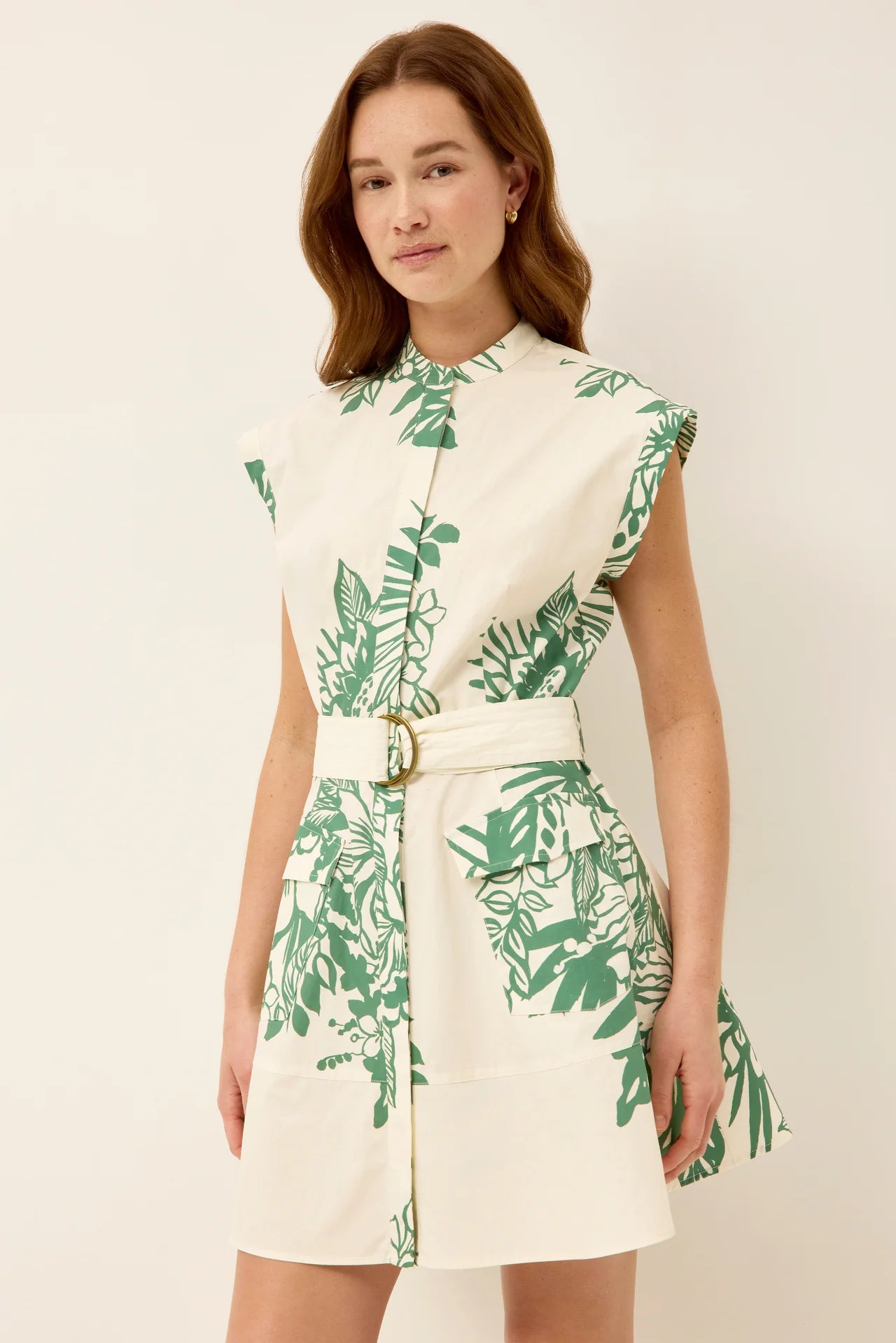 Woman wearing a white dress with green leaf pattern on a plain background.