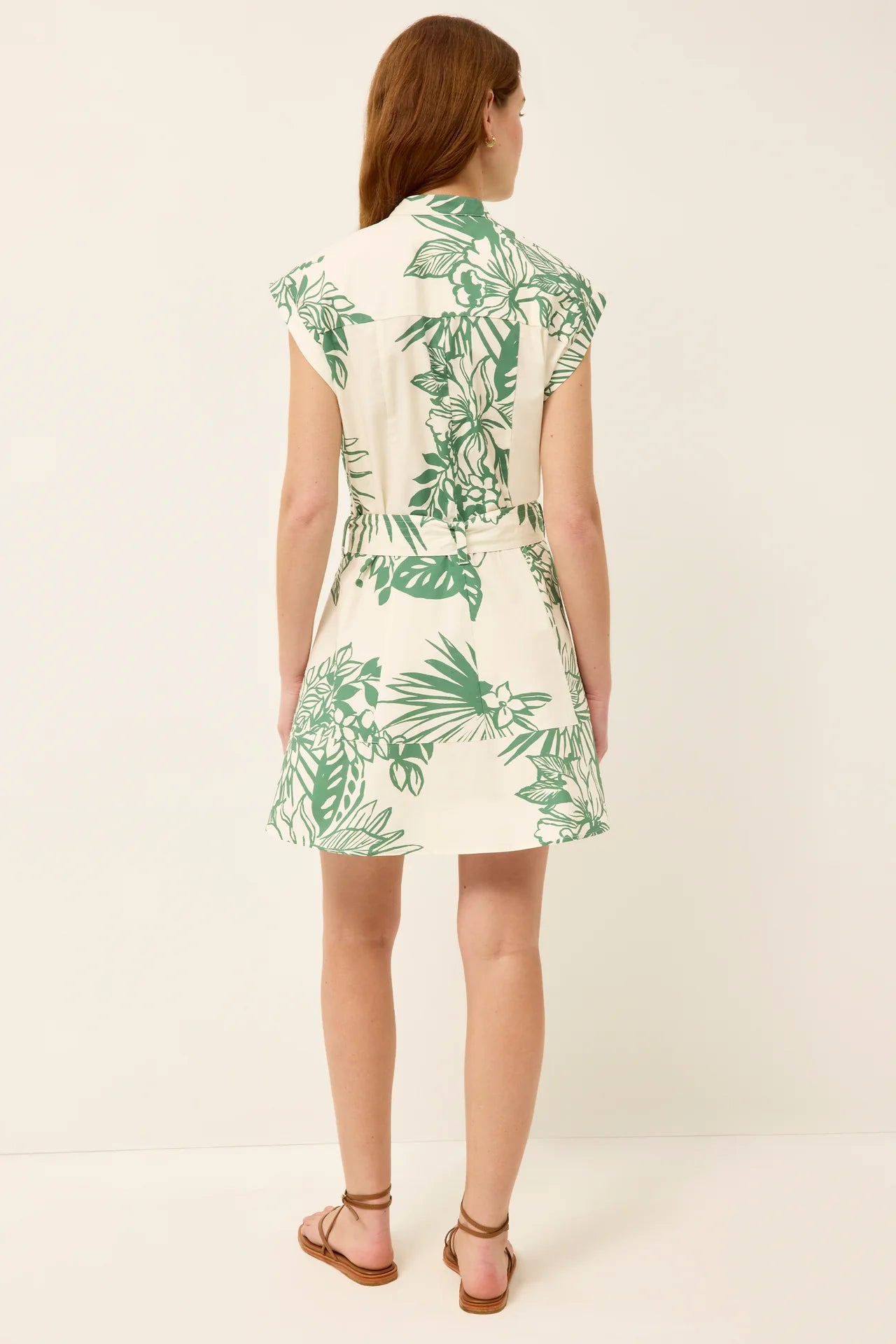 The back of a woman wearing a white dress with green leaf pattern on a plain background.
