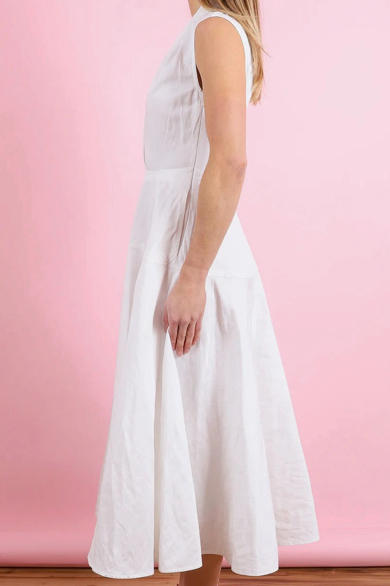 Side view of a woman wearing an off-white dress agianst a pink background.