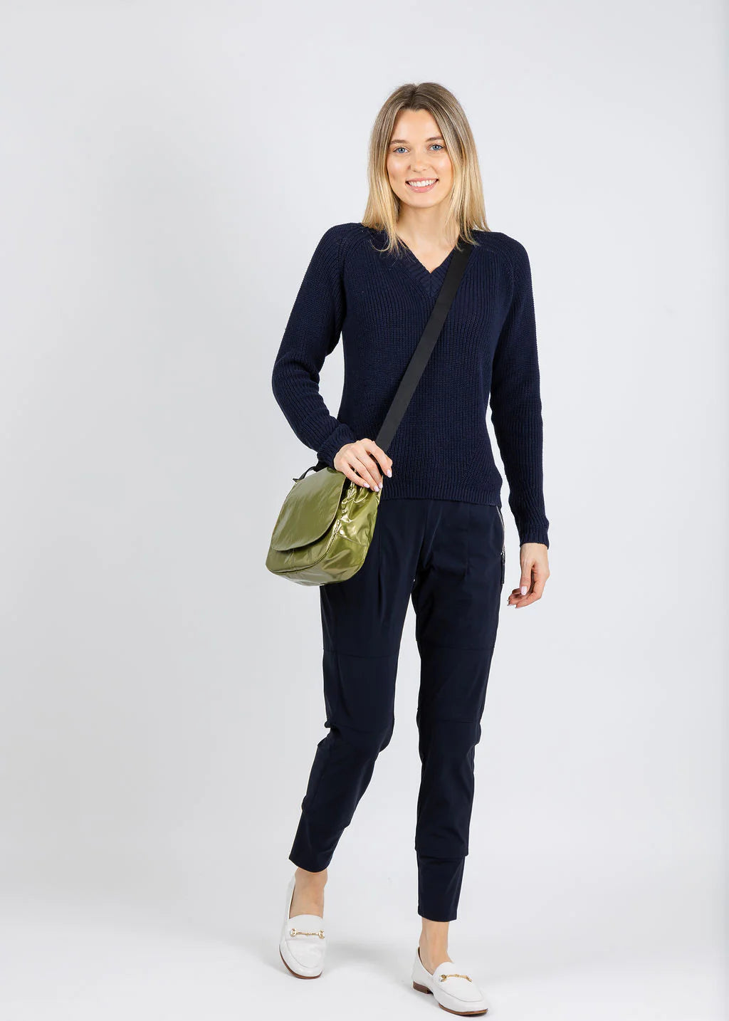 Woman wearing a navy blue outfit with a green bag on a white background