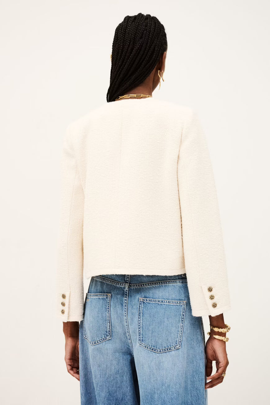 Back of a woman wearing a white jacket with gold buttons and blue jeans on a white background.