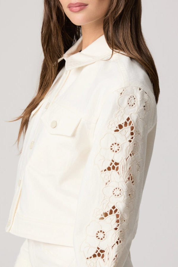 Close-up of a ecru denim jacket with lace detailing on a plain background.