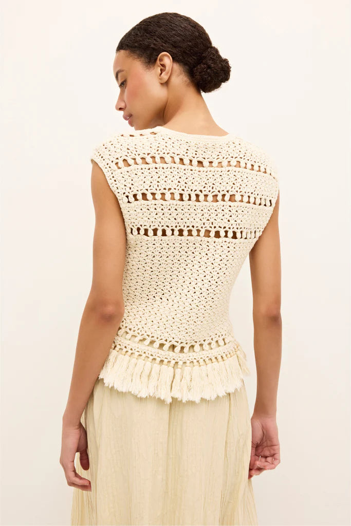 Woman wearing a beige crochet top with a plain background.