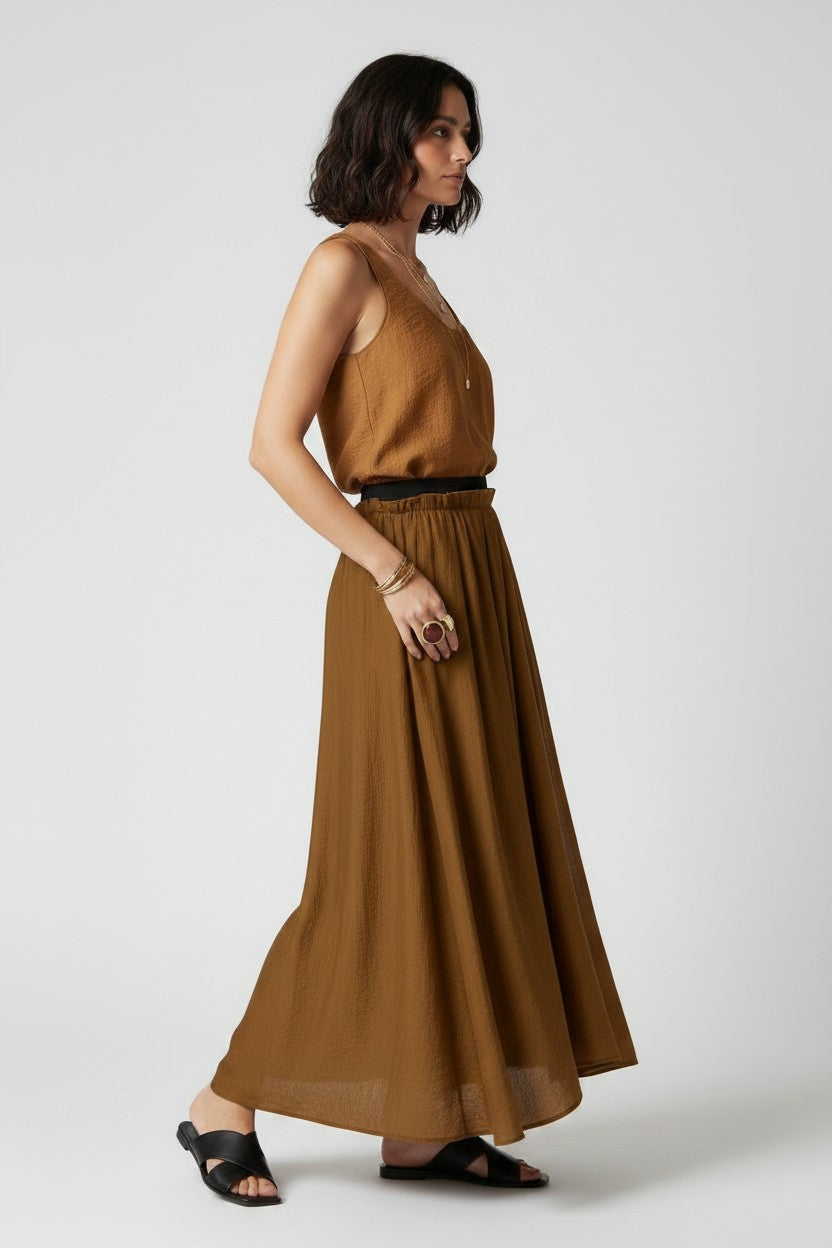 Woman wearing a brown outfit with black shoes and gold jewelry on a white background.