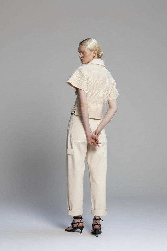 Back of a woman wearing a beige outfit standing against a plain background.
