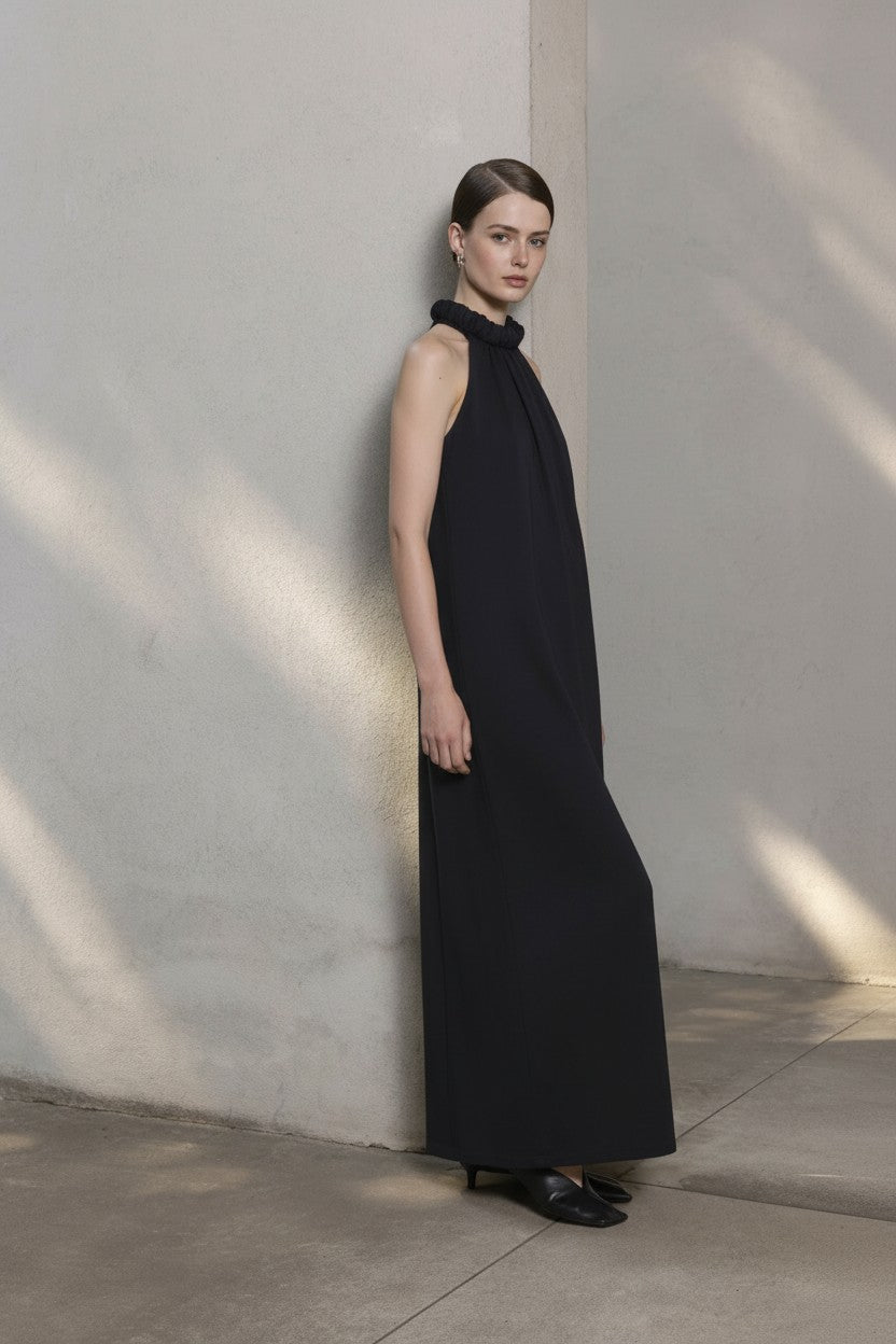 Woman wearing a black sleeveless dress against a light gray wall.