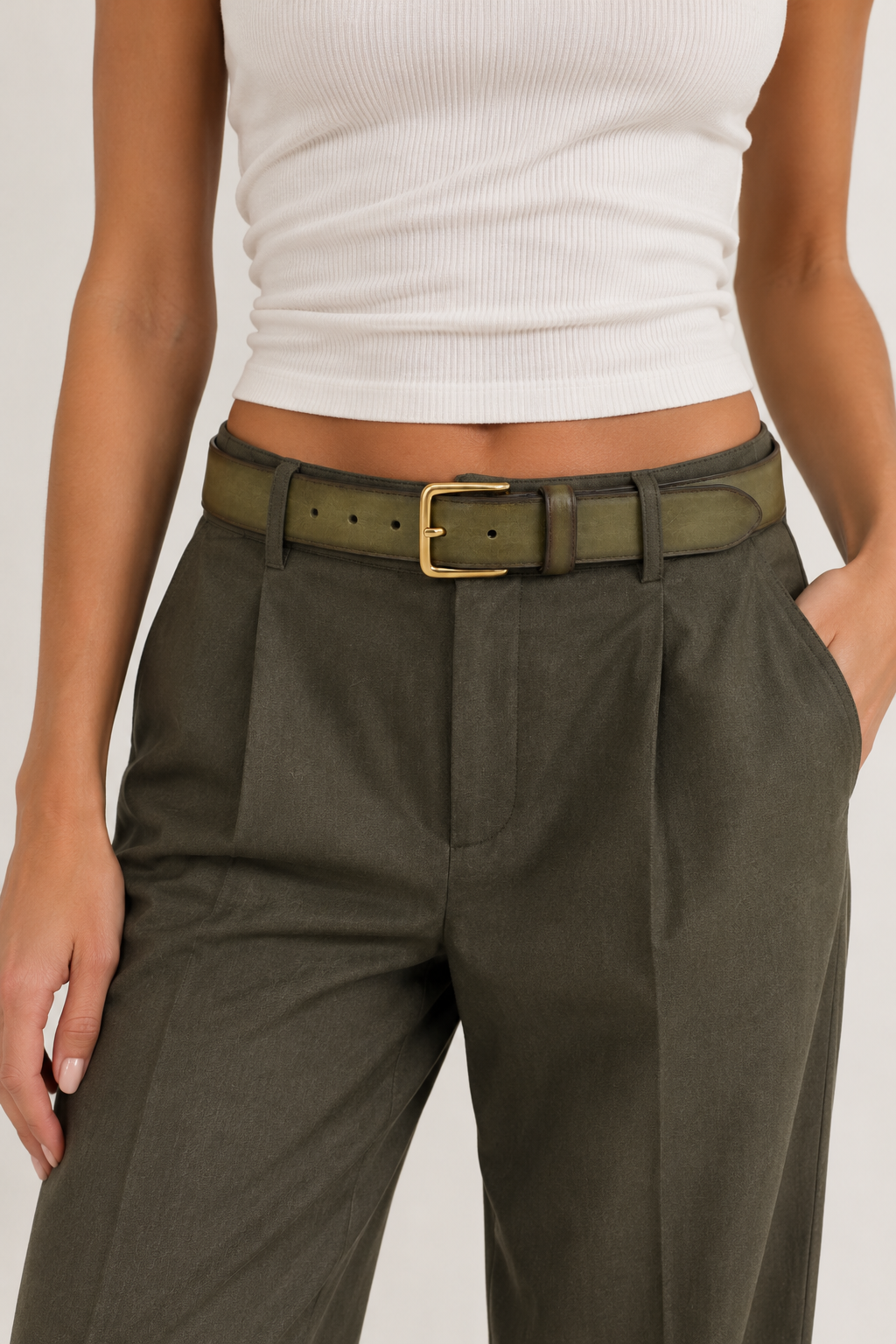 Model wearing an olive green leather belt with a gold-tone rectangular buckle, styled with dark olive tailored trousers and a white ribbed top.