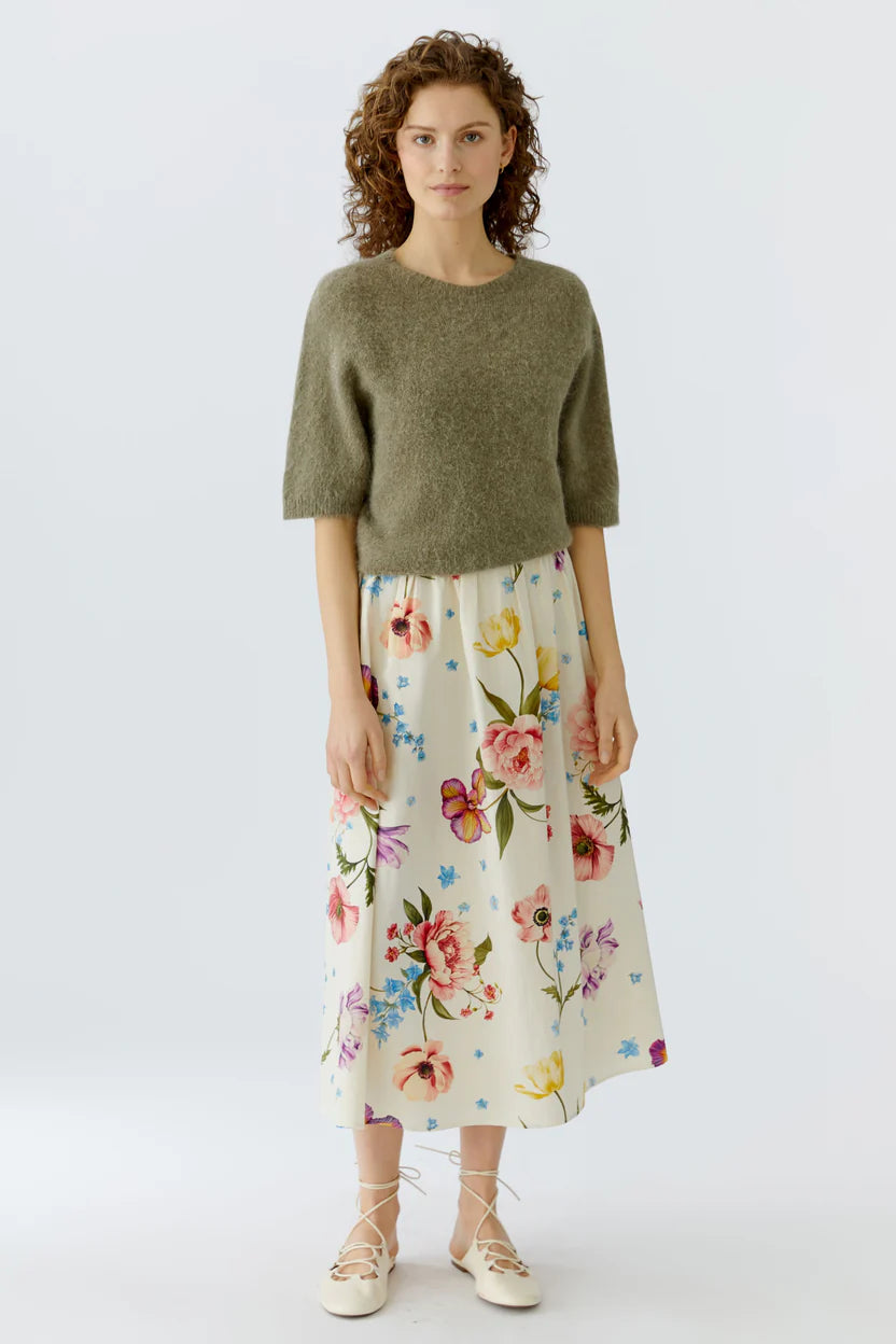 Woman wearing a green sweater and floral skirt on a white background.