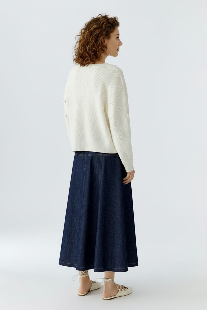 The back of a woman wearing a white sweater and dark blue skirt on a white background.