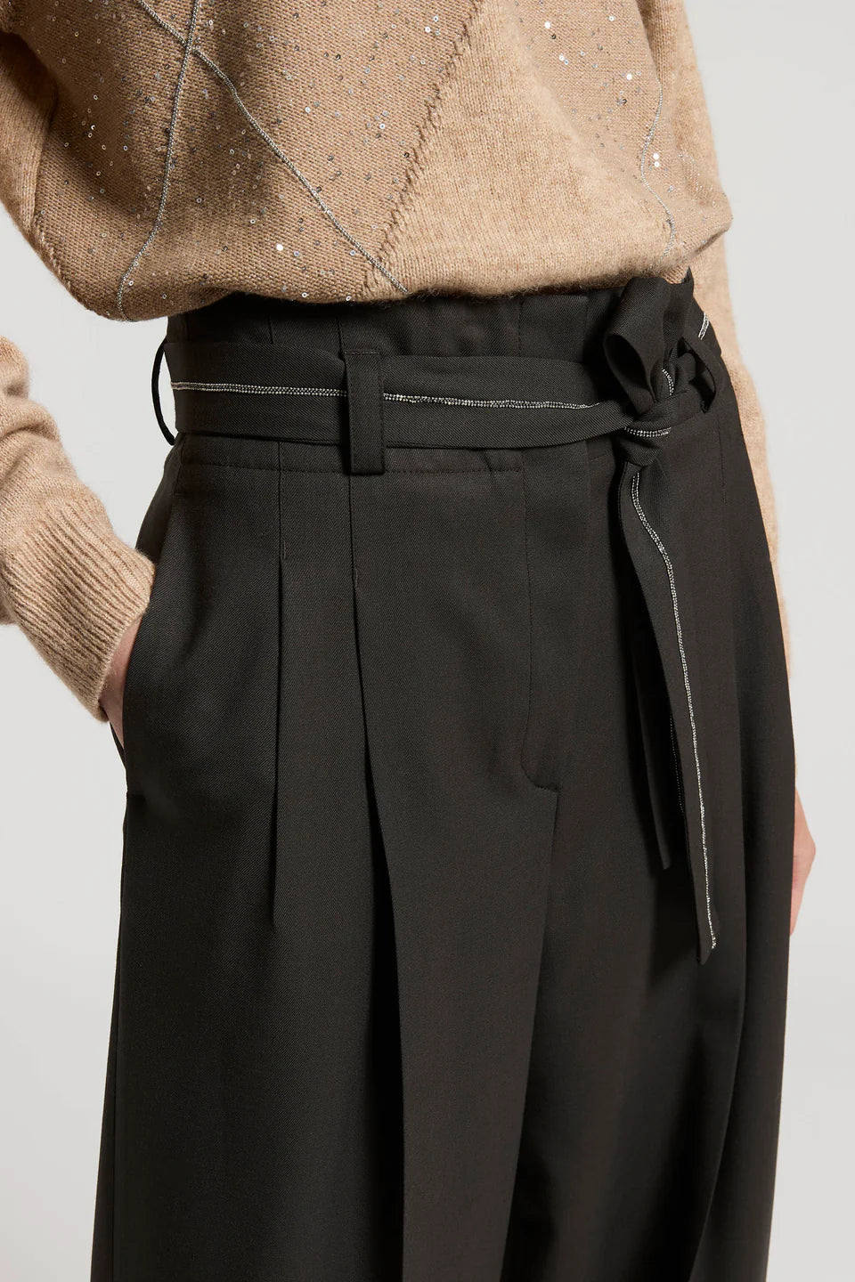 Black pleated pants with a belt worn by a person on a light gray background.