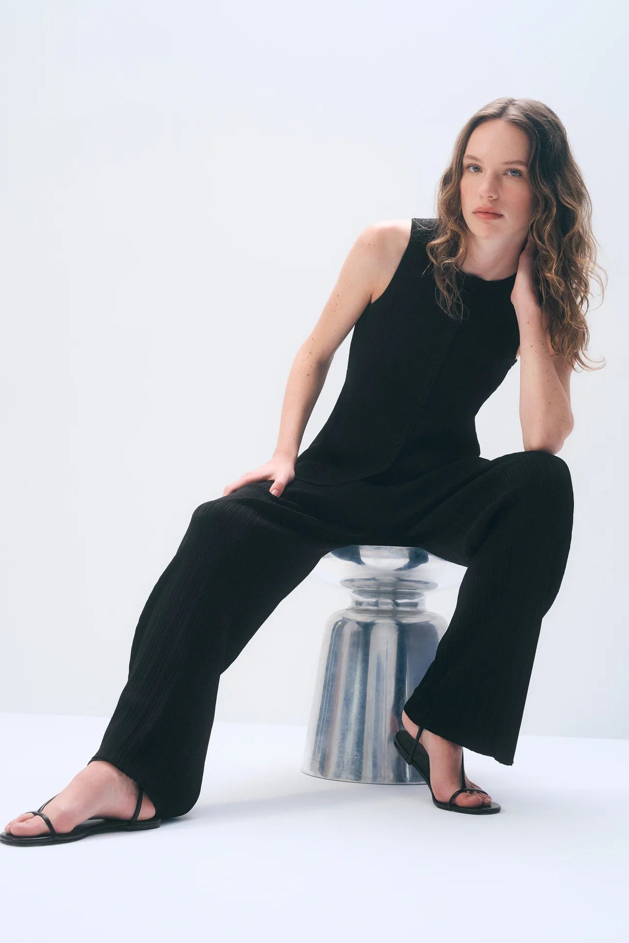 Woman wearing a black sleeveless top with matching pants sitting on a white background.
