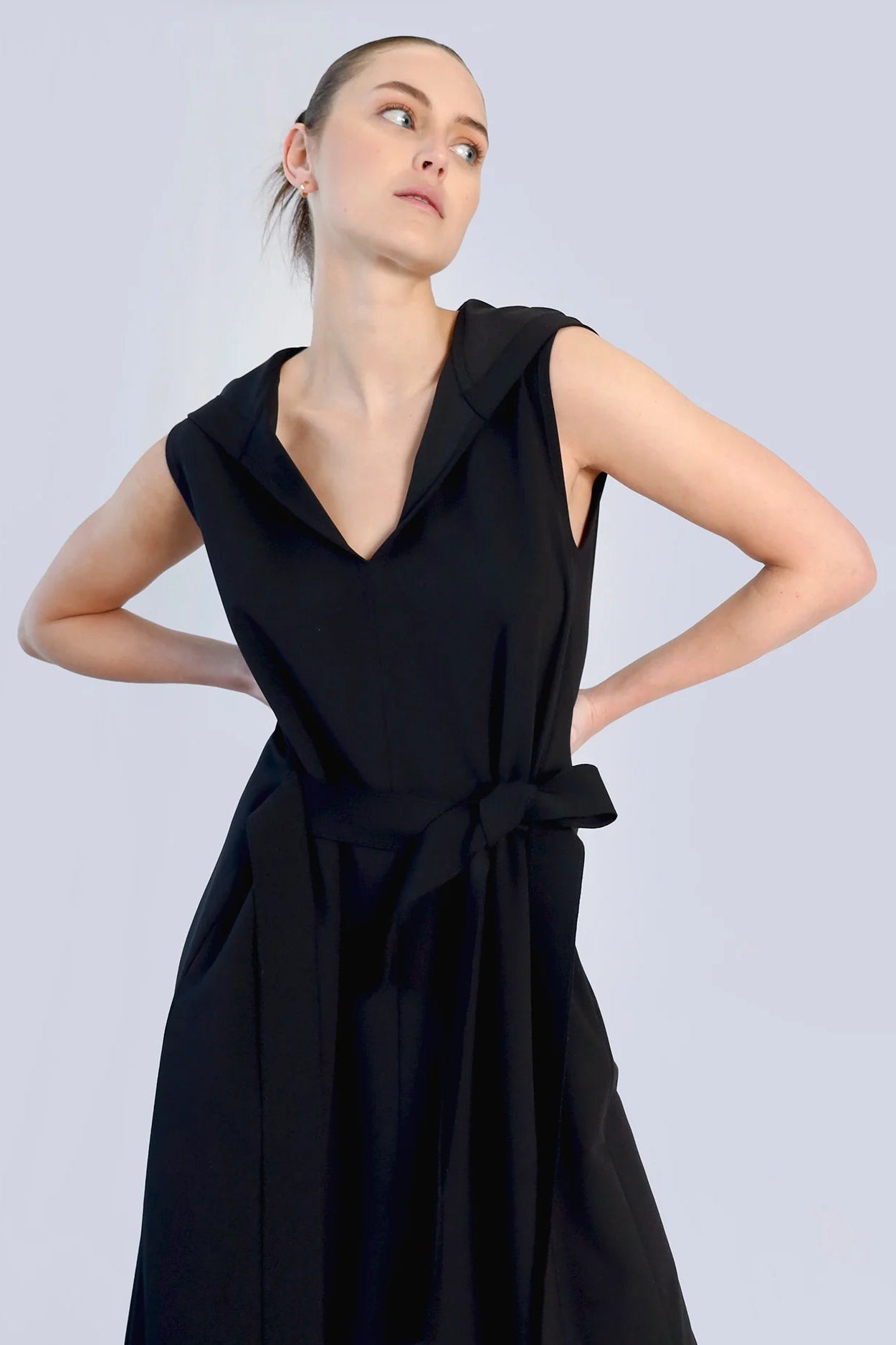 Close-up of a woman wearing a black sleeveless dress with a tie front on a grey background.