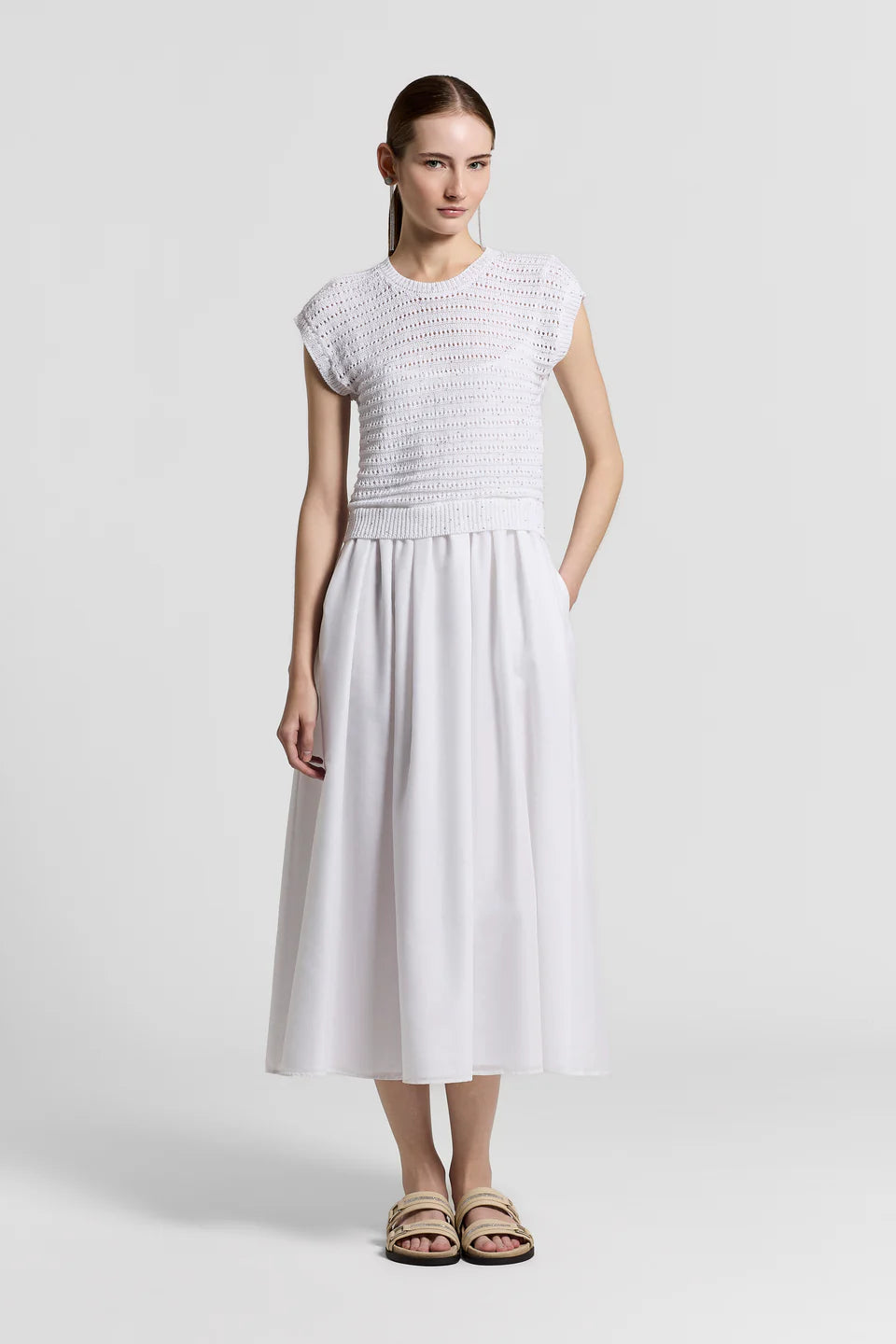 Woman wearing a white dress with a textured top and flowing skirt on a light gray background.