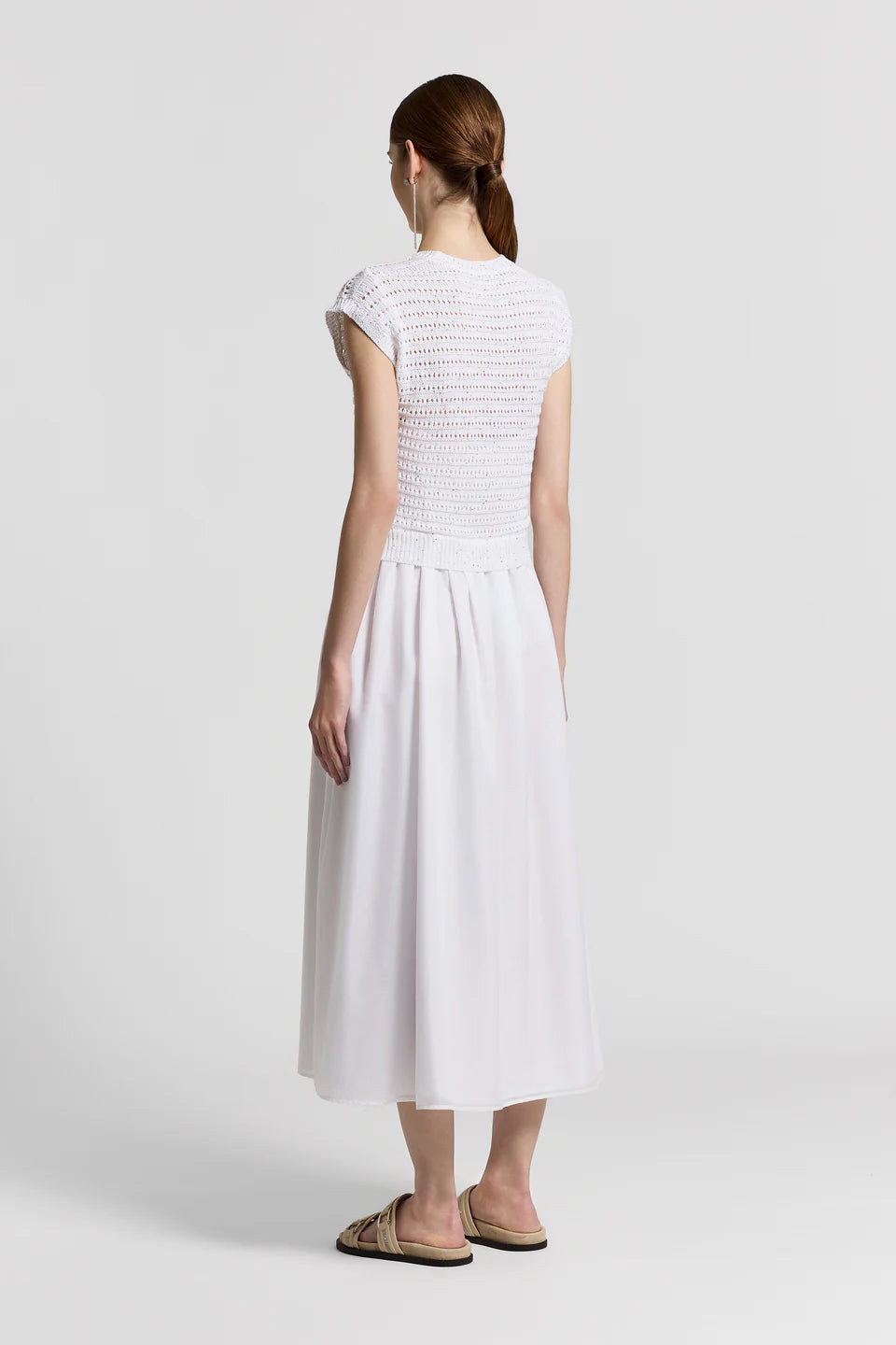 The back of a woman wearing a white dress with a textured bodice on a plain background.