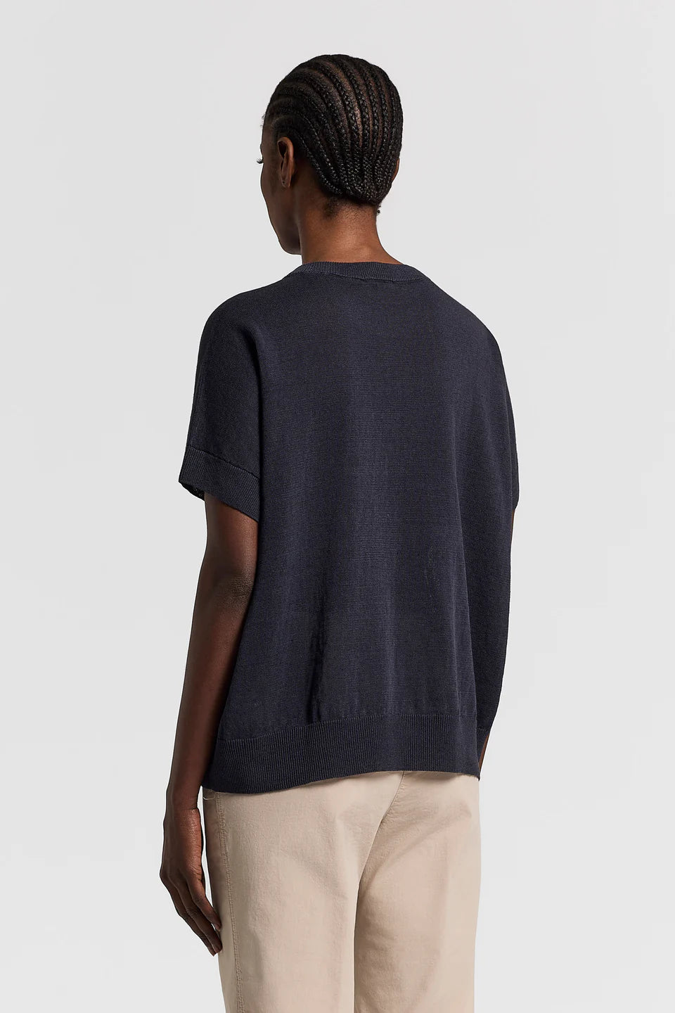 The back of a woman wearing a navy blue t-shirt and beige pants on a light gray background.