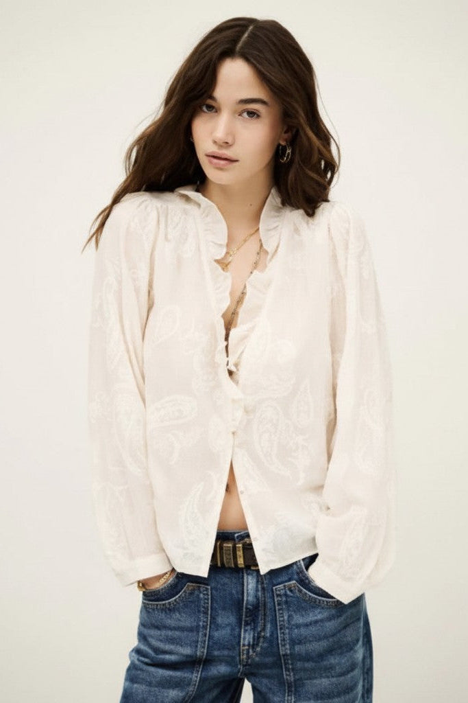 Woman wearing a white blouse and blue jeans against a plain background.