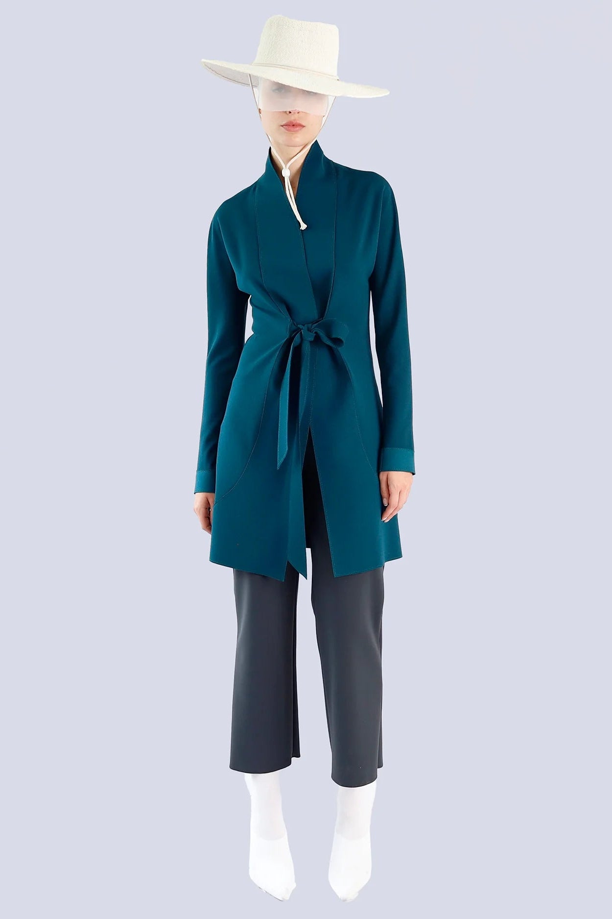 Person wearing a teal wrap cardigan and gray pants on a plain background.