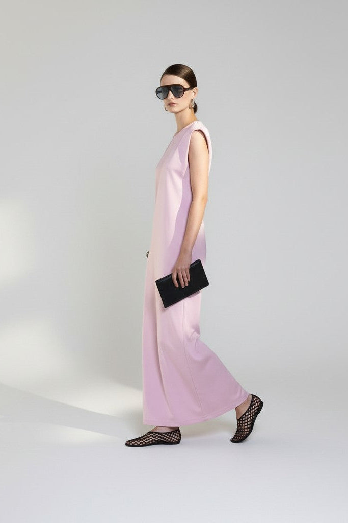 Woman wearing a light pink sleeveless dress and black shoes on a white background.