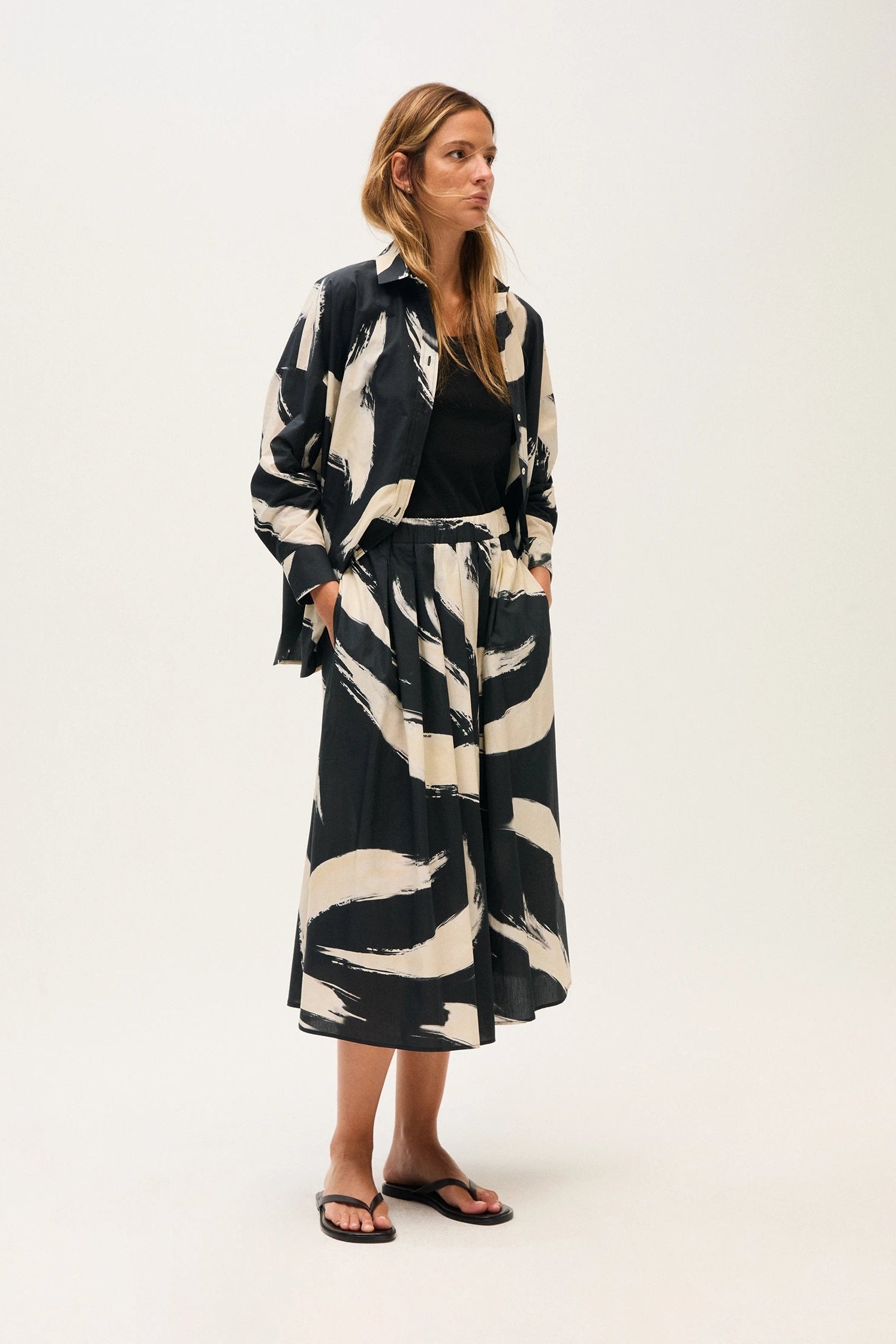 Woman wearing a black and off-white patterned blouse and skirt on a white background.