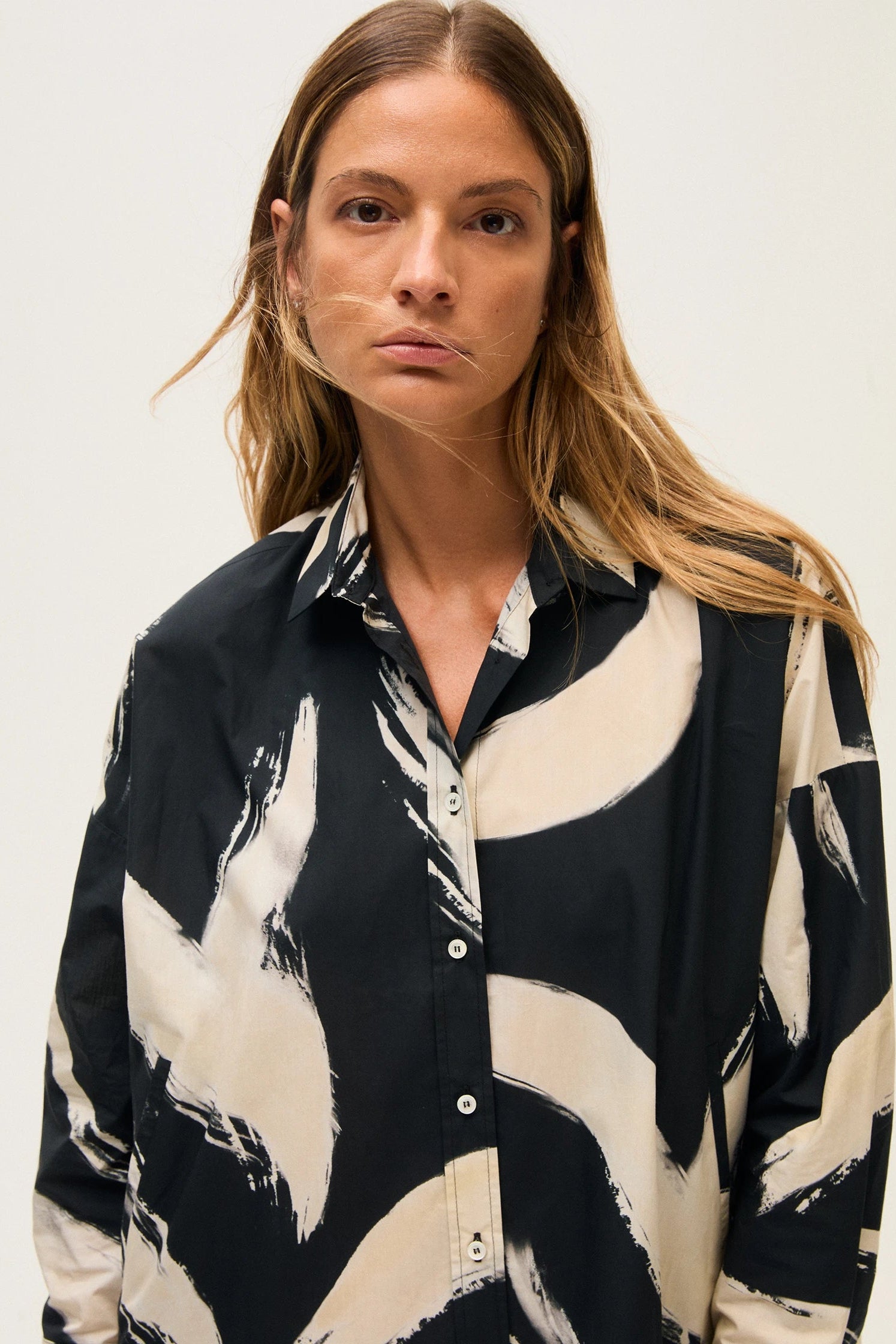 Close-up of a woman wearing a black and off-white patterned shirt against a plain background.