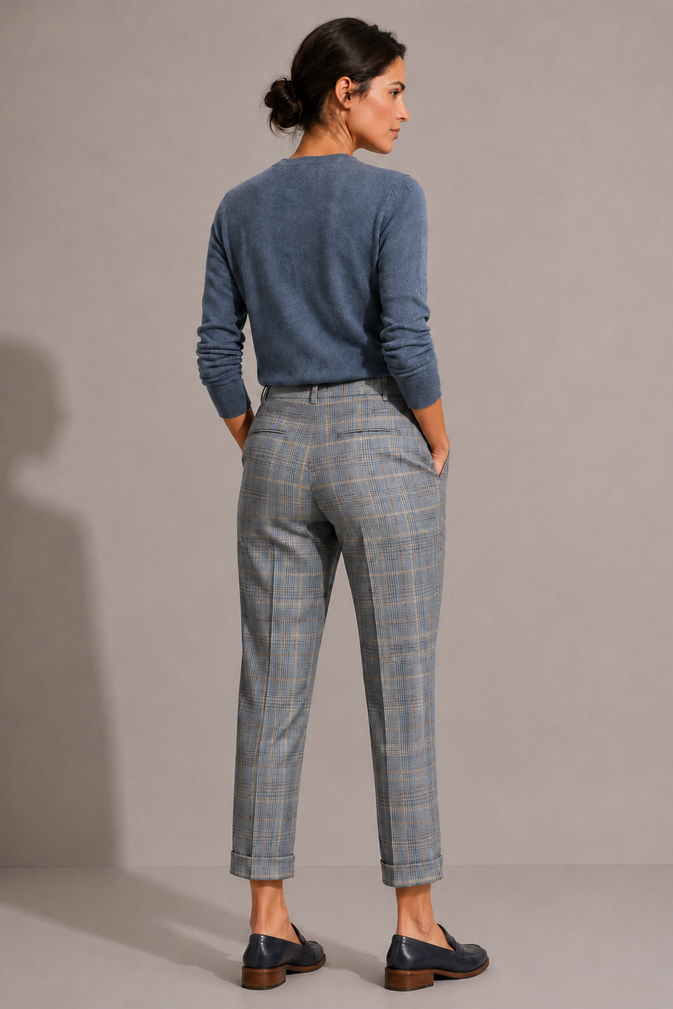 Model wearing the blue-gray plaid Maura Pant, shown from the back with welt pockets, belt loops, and cuffed hems.