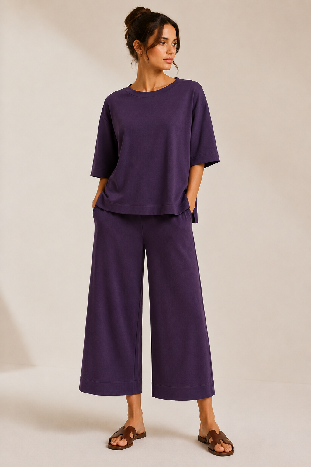 Model wearing the QL2 Costanza two-piece set in deep plum, styled untucked with wide-leg cropped pants and brown sandals.