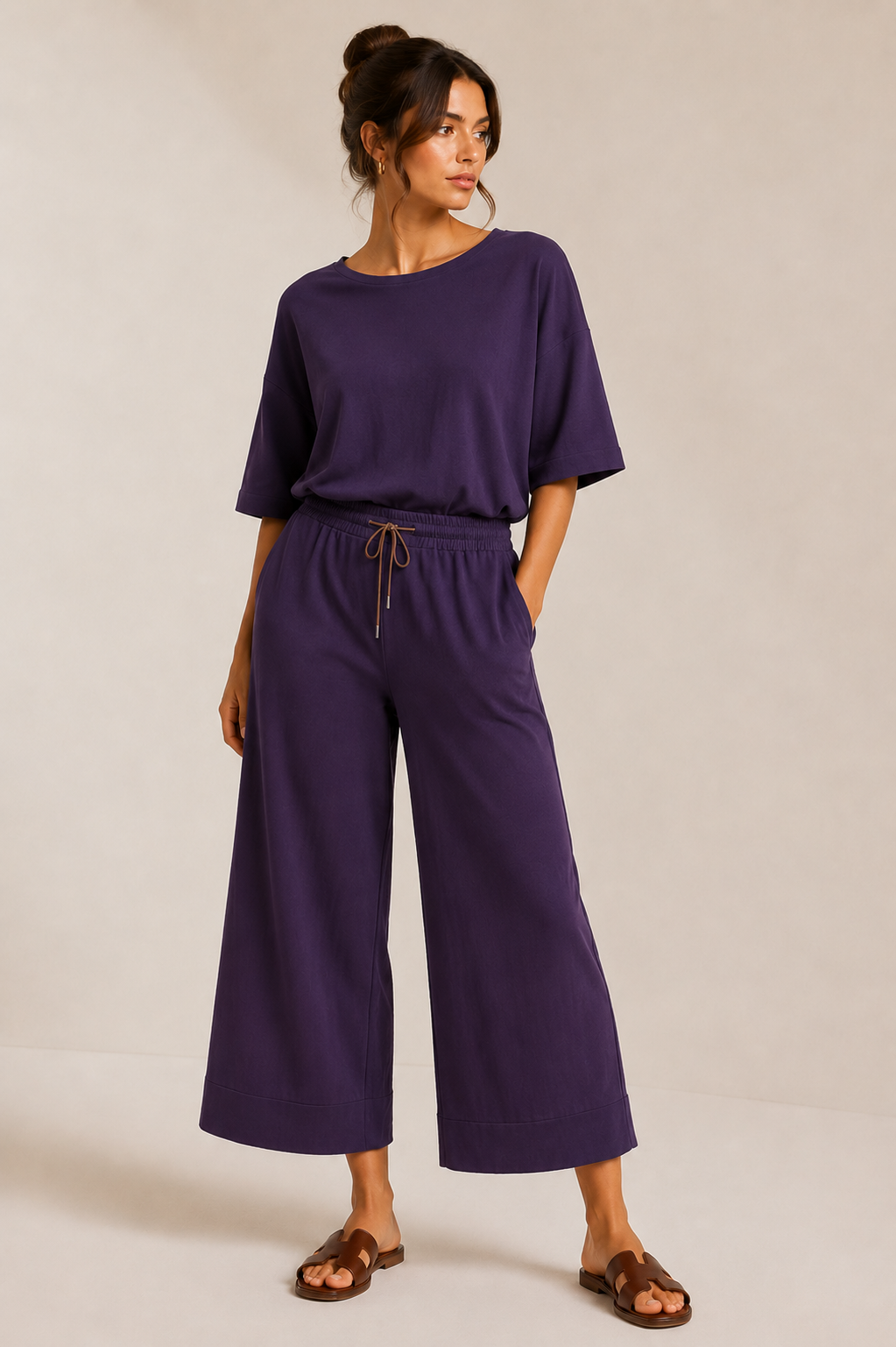 Model wearing the QL2 Costanza two-piece set in deep plum, with the relaxed top tucked into the elastic drawstring waist of the wide-leg cropped pants.