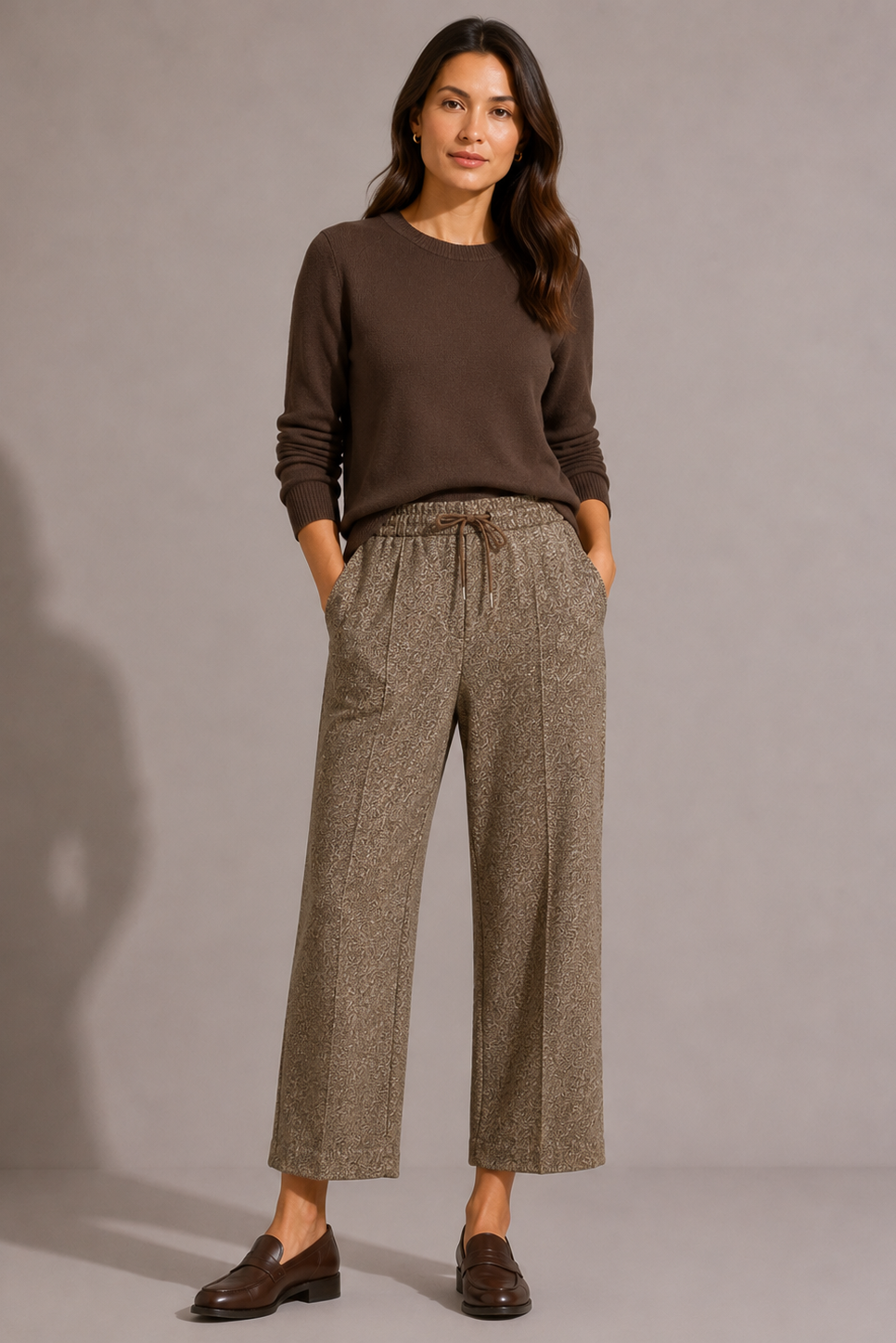 Model wearing the QL2 Tilde Wool Pant in brown mélange, styled with a dark brown crewneck sweater and brown loafers, front view.