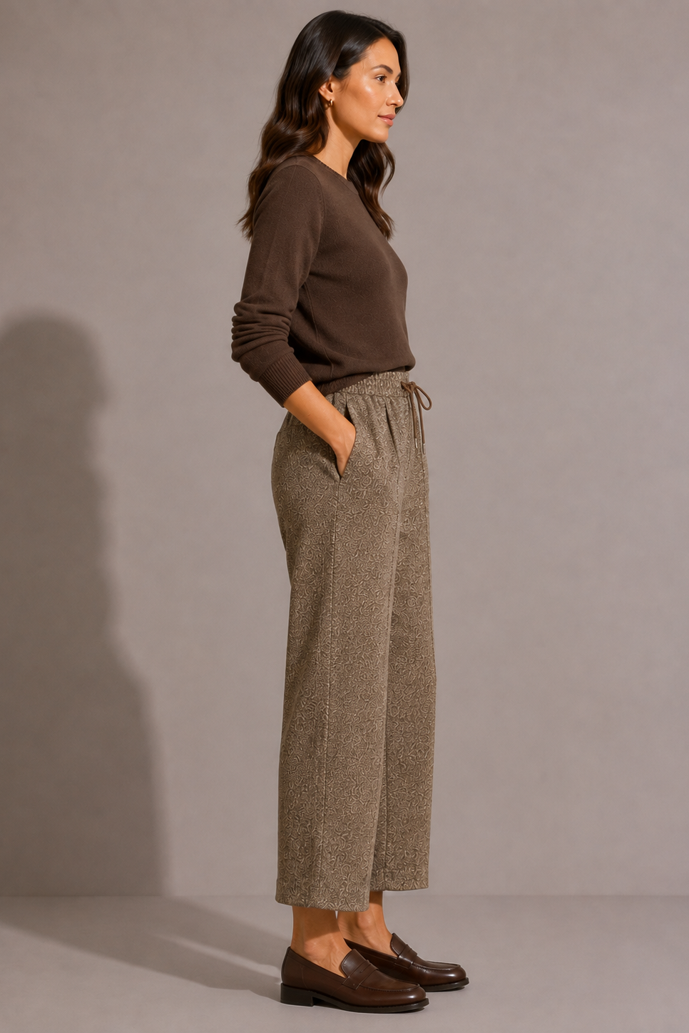 Side view of model wearing the QL2 Tilde Wool Pant in brown mélange, styled with a dark brown crewneck sweater and brown loafers.