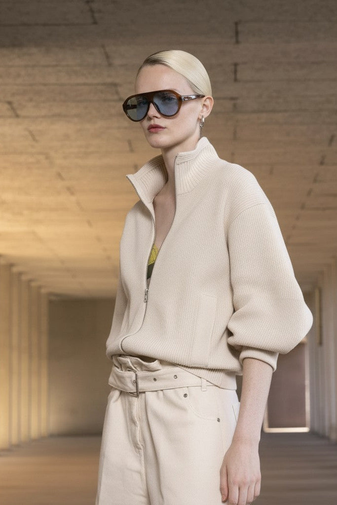 Woman wearing sunglasses and a beige outfit in a architectural setting.