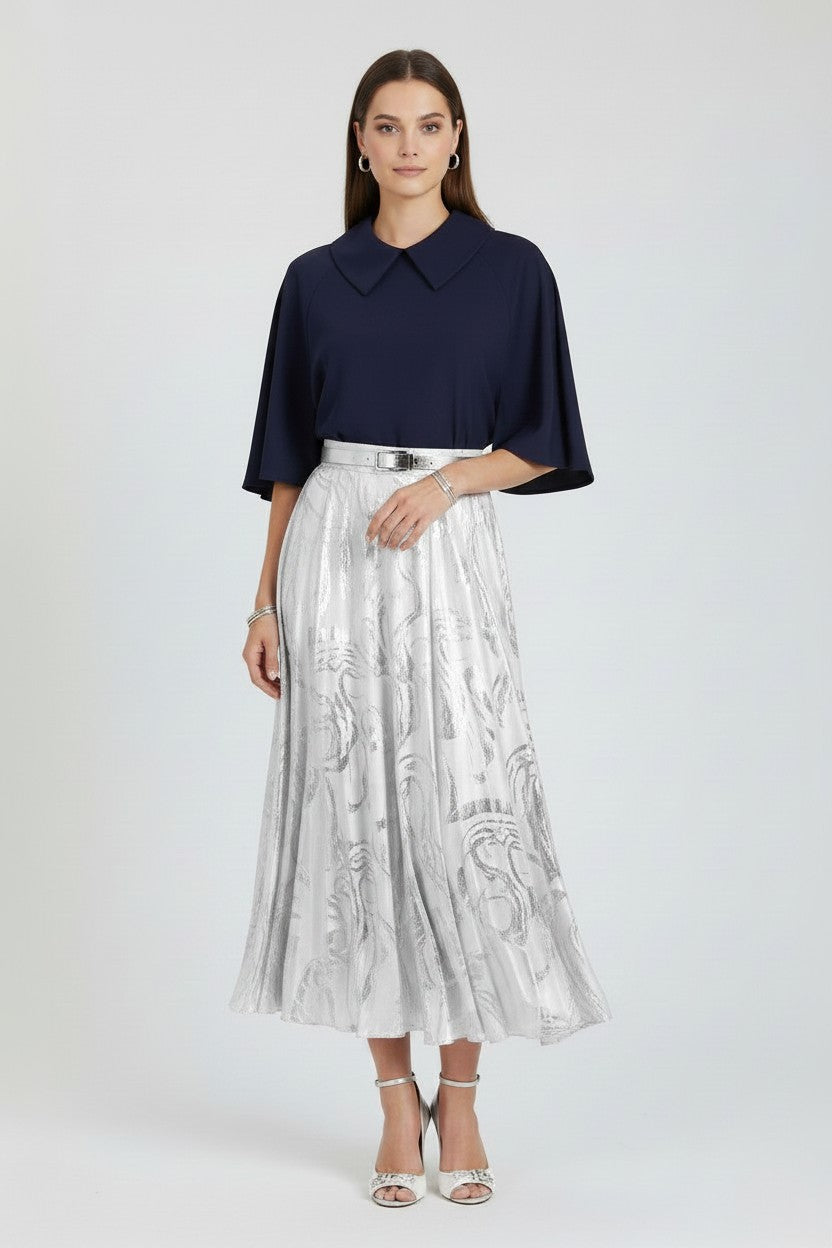 Woman wearing a navy top and silver pleated skirt on a white background.