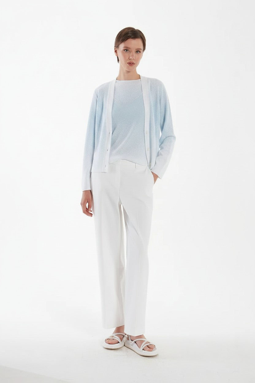 Woman wearing a light blue cardigan over a matching top and white pants on a white background.